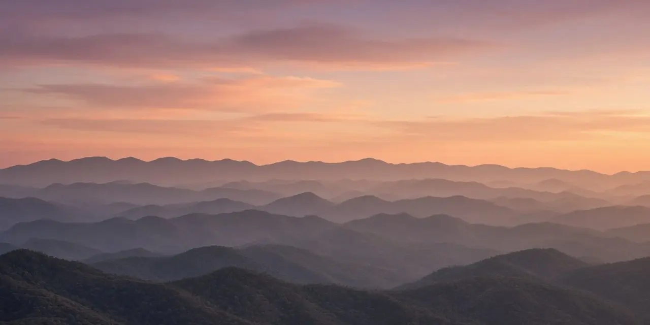 Layered mountain ranges fading into gentle haze beneath a warm sunset sky