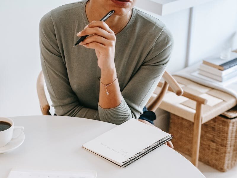 High angle crop professional female psychotherapist with pen and notepad listening attentively to client during psychotherapy session in light studio